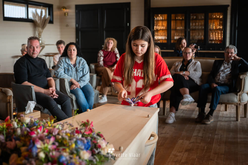 Kind legt een persoonlijke herinnering op de uitvaartkist tijdens een intieme afscheidsceremonie, vastgelegd door een afscheidsfotograaf.